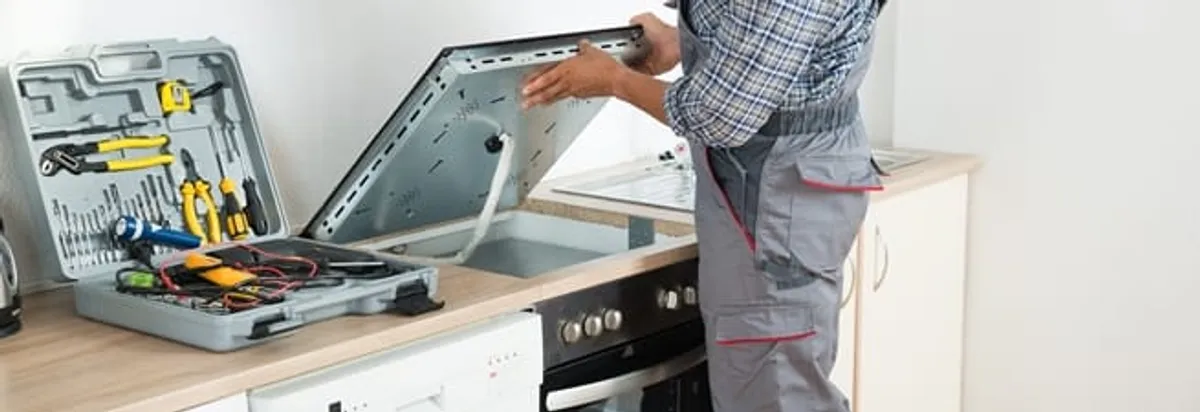 Cooktop repair technician lifting a built-in stovetop for service in Reno, NV