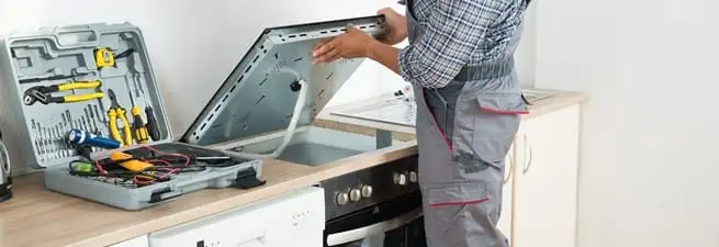 Cooktop repair technician lifting a built-in stovetop for service in Reno, NV