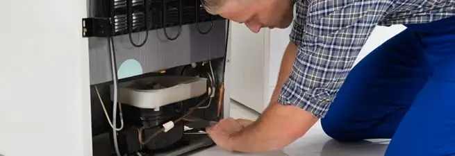 Refrigerator repair technician servicing the compressor and condenser area in Reno, NV