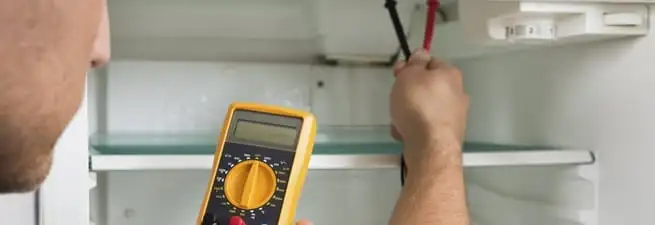 Refrigerator repair technician testing electrical components with a multimeter in Reno, NV