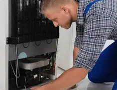 Refrigerator repair technician servicing the compressor and condenser area in Reno, NV